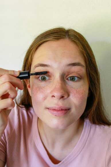 A young woman applies mascara to her eyelashes.